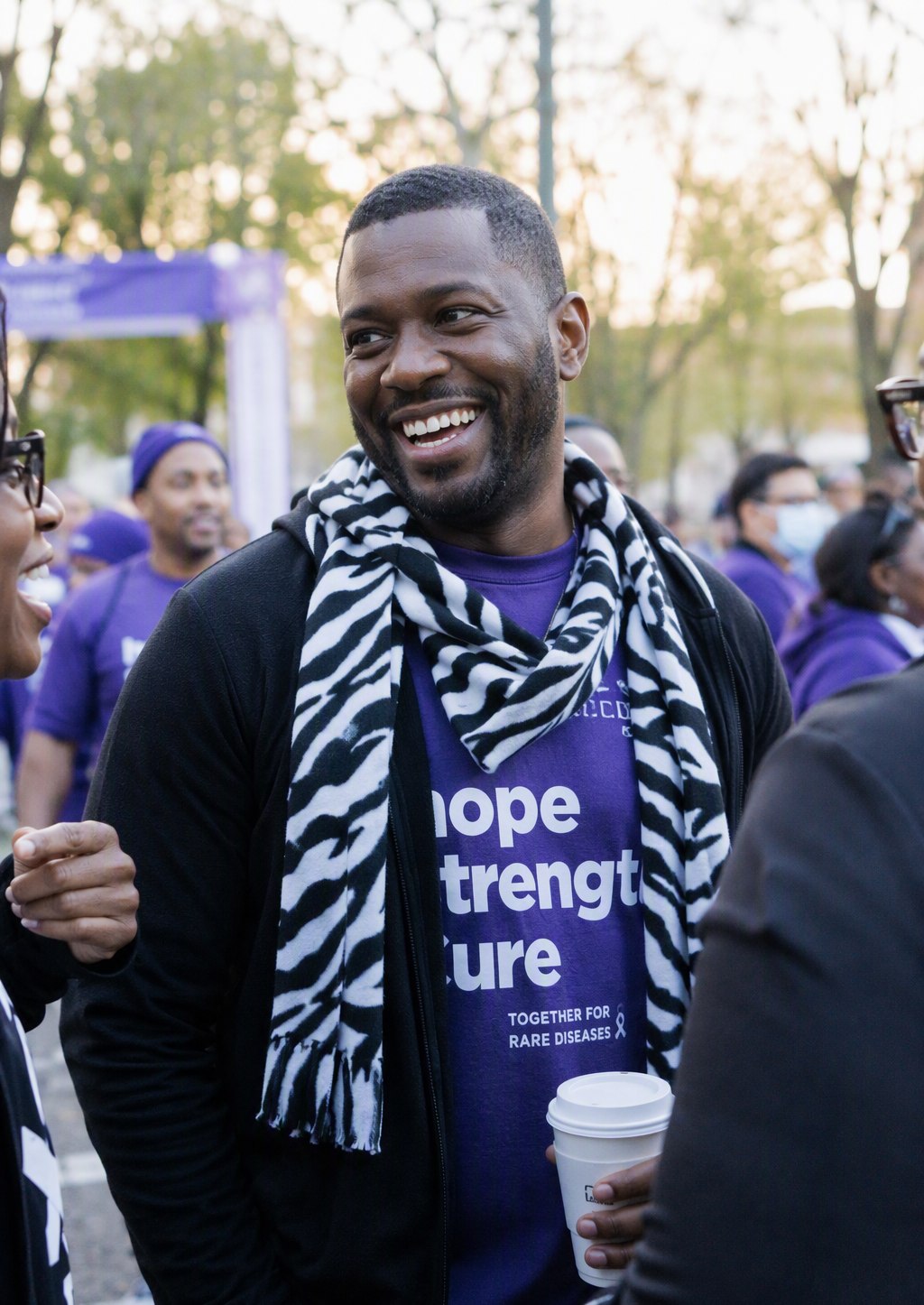 A father wearing a zebra-print scarf at a rare disease awareness walk, laughing with friends